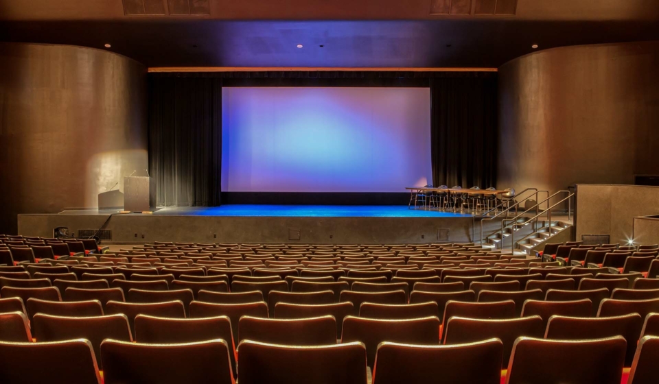 Empty auditorium with all lights on. Visible scrren in the center of stage.